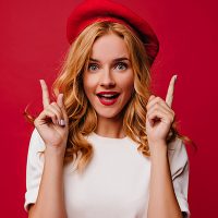 Ecstatic white girl in beret posing with amazement. Elegant caucasian female model in t-shirt standing on red background.